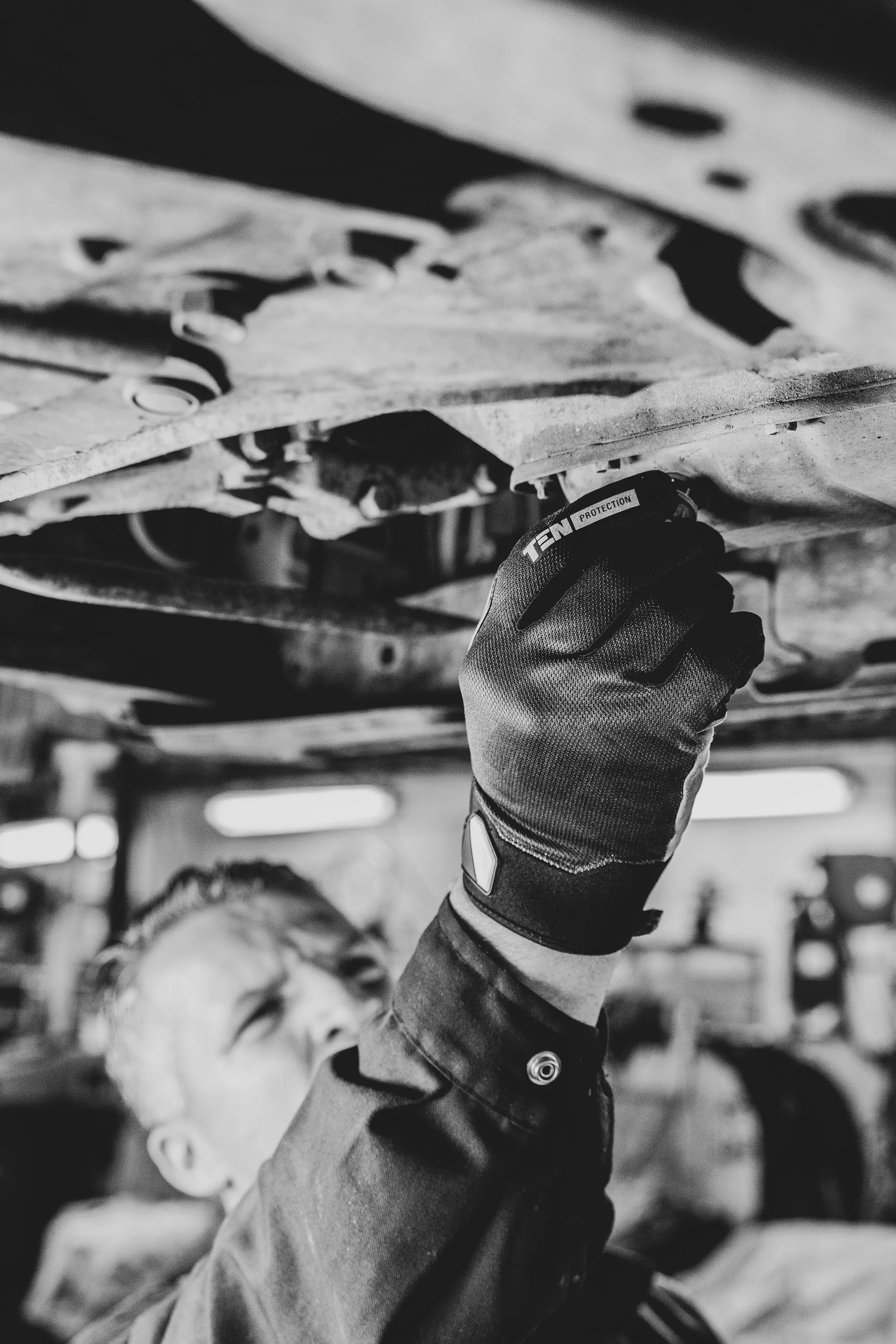 Mechanic in protective gear examining the underside of a vehicle