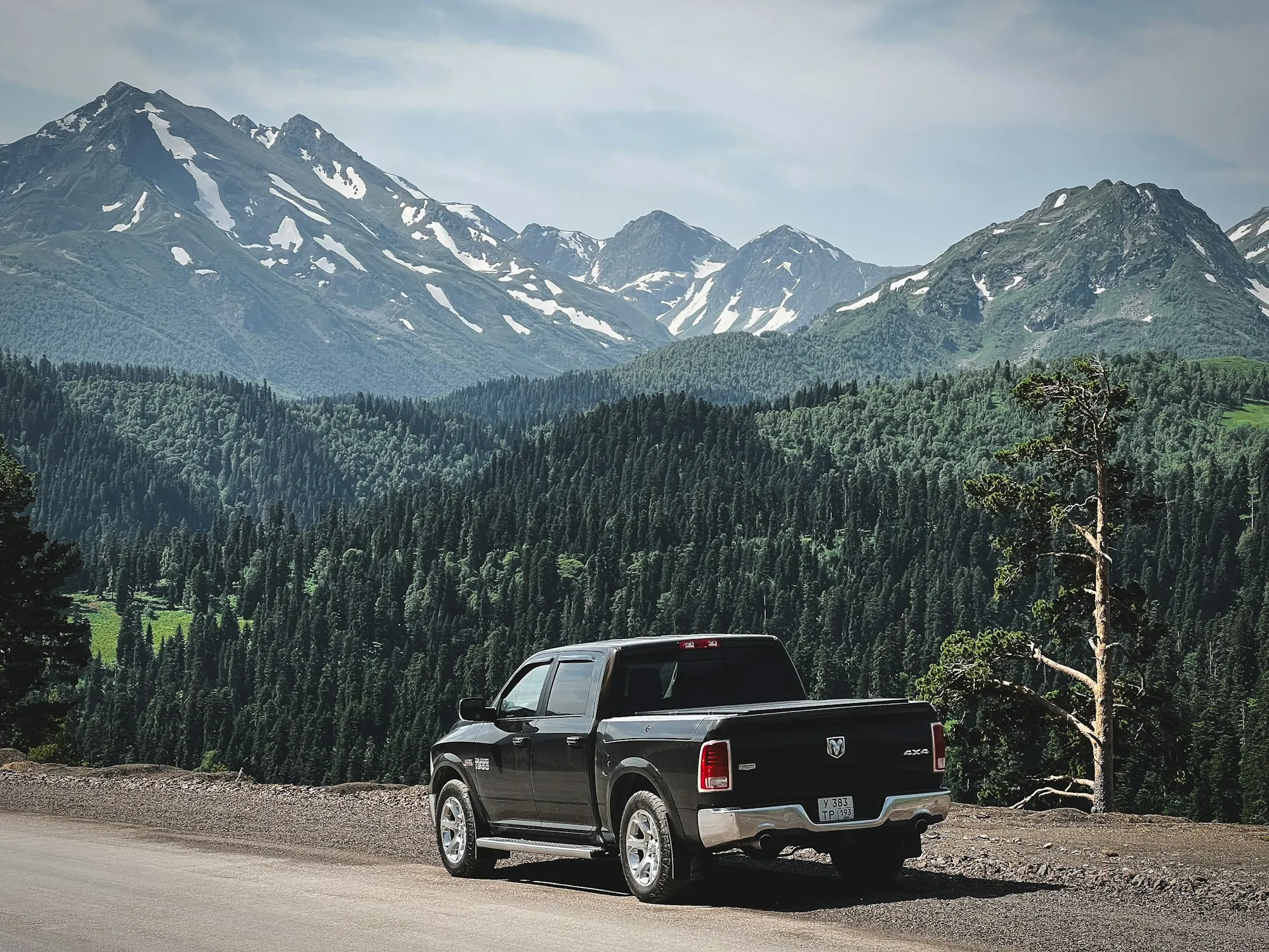 Dark pickup truck on a mountain road with snowy peaks behind