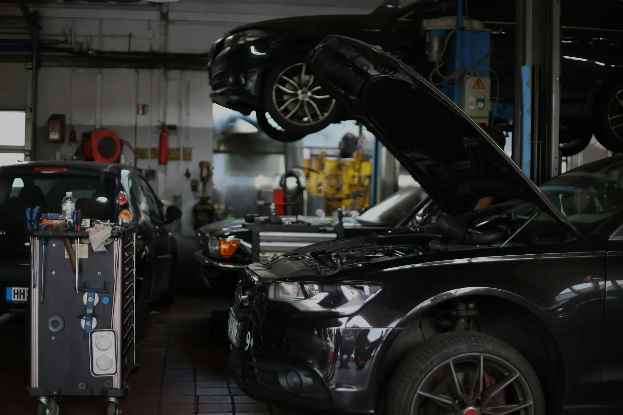 Repair shop bay with a dark sedan raised and its hood open